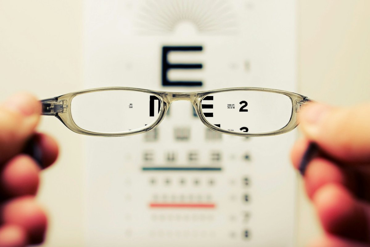Une paire de lunettes tenue devant une échelle de lecture floue