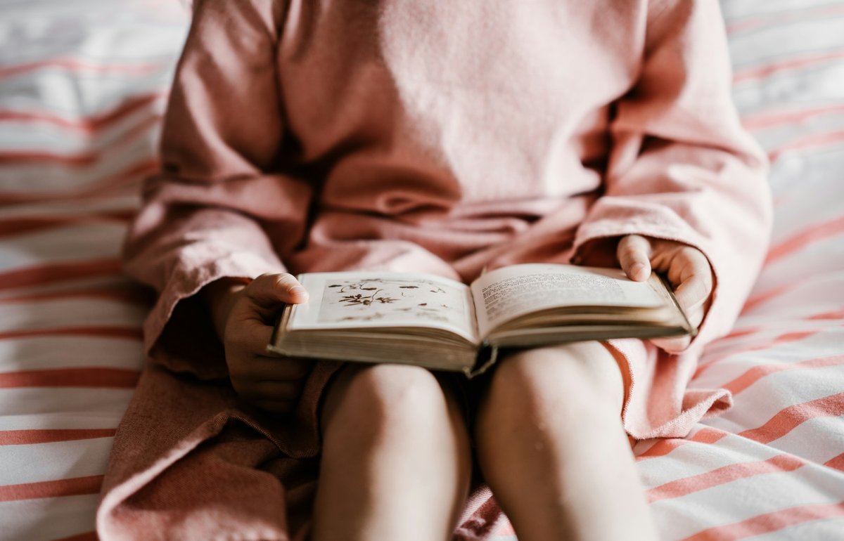 Mains d'un enfant tenant un livre illustré ouvert, visage hors du cadre