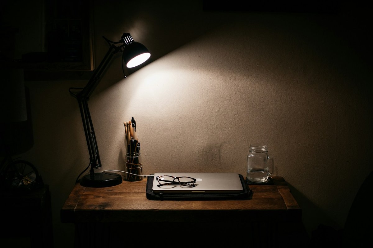 Lampe de bureau allumée la nuit au-dessus d'un carnet et d'une paire de lunettes